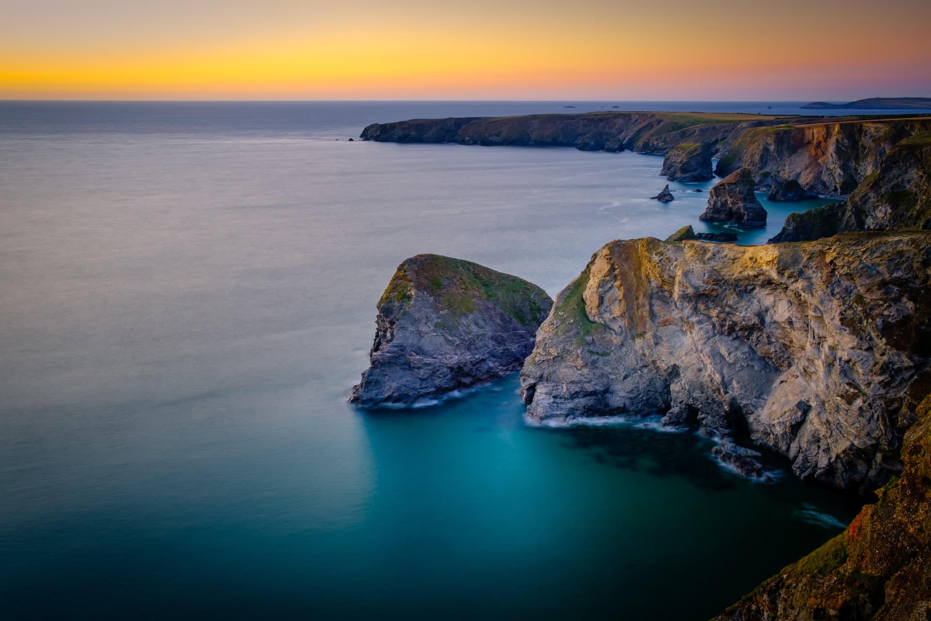 Coastal cliffs meeting turquoise sea at sunset, Mawgan Porth, Cornwall.