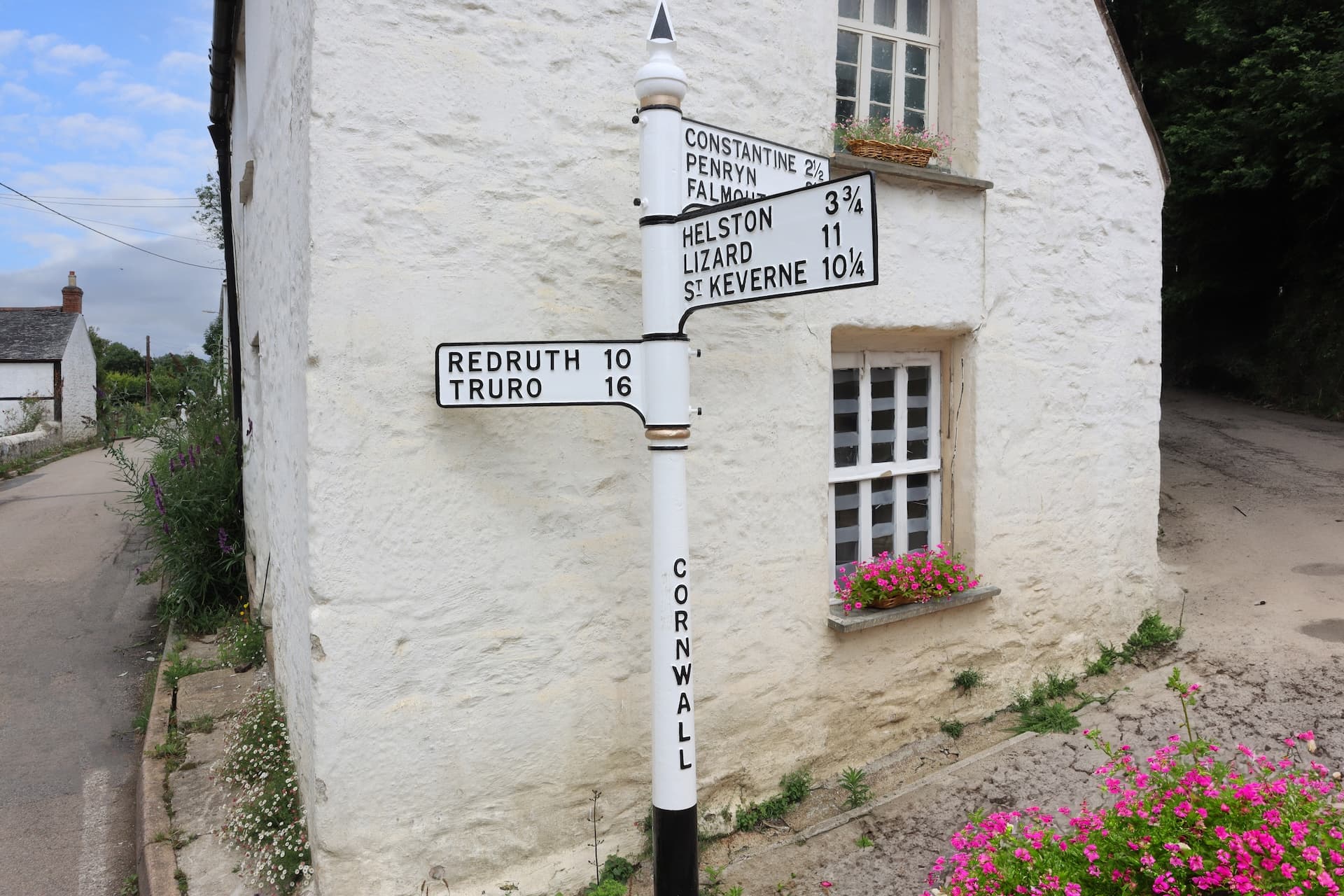 White directional signpost with distances to Redruth and Truro outside a whitewashed cottage in Cornwall.