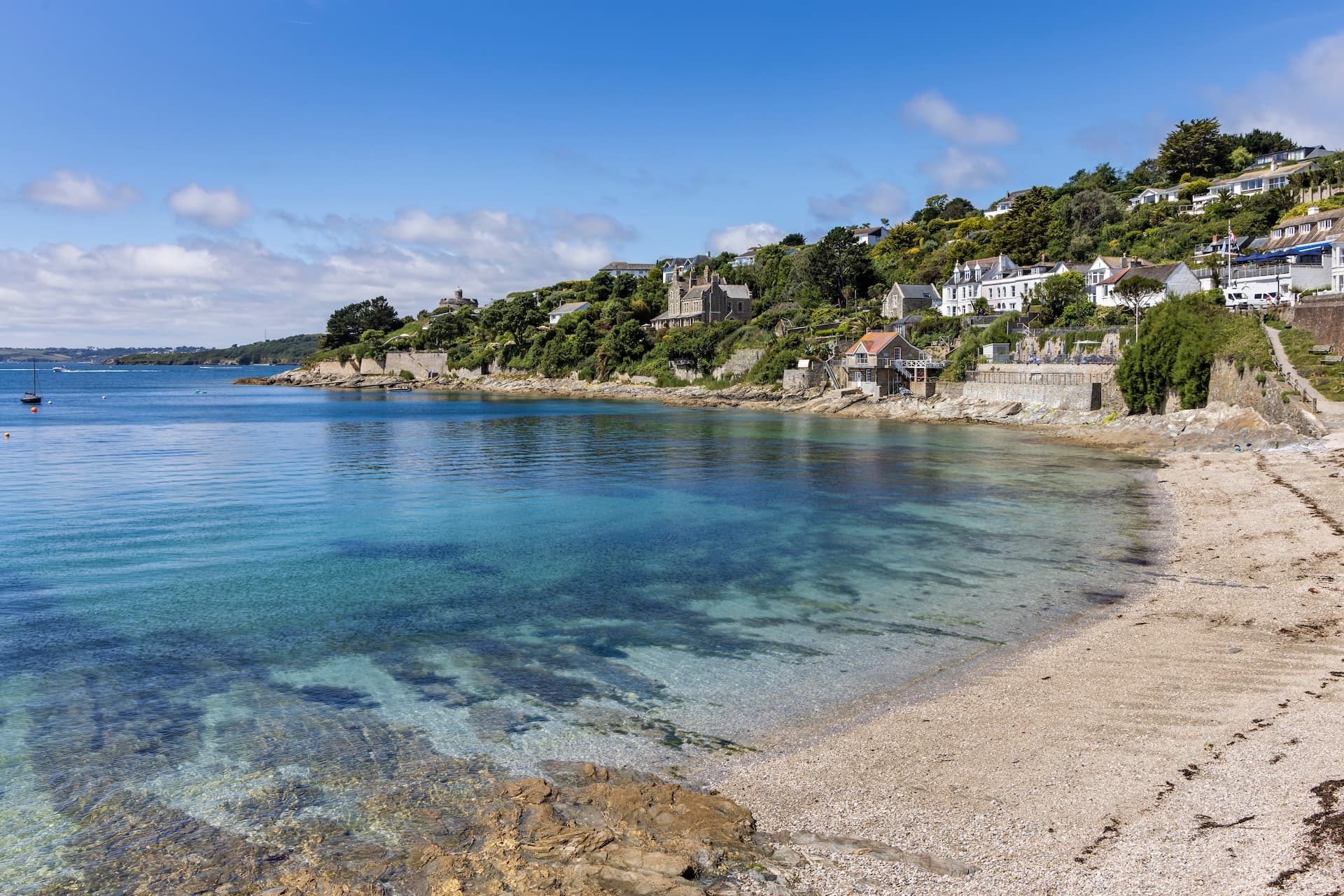 Clear turquoise water meets a pebble beach below houses built into a lush green hillside at Roseland Peninsula.