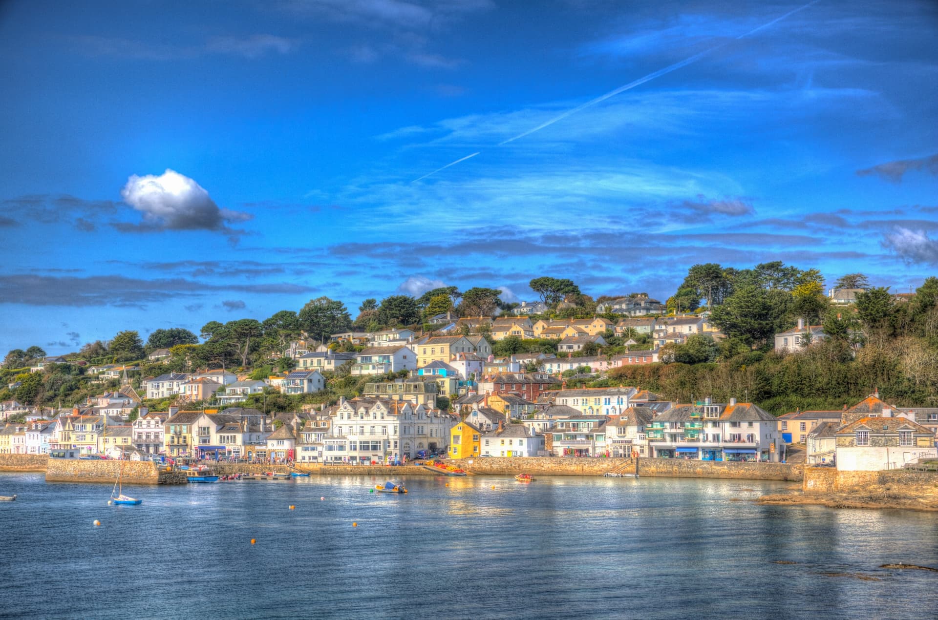Coastal village with colorful houses on a hillside above a harbor under a bright blue sky.