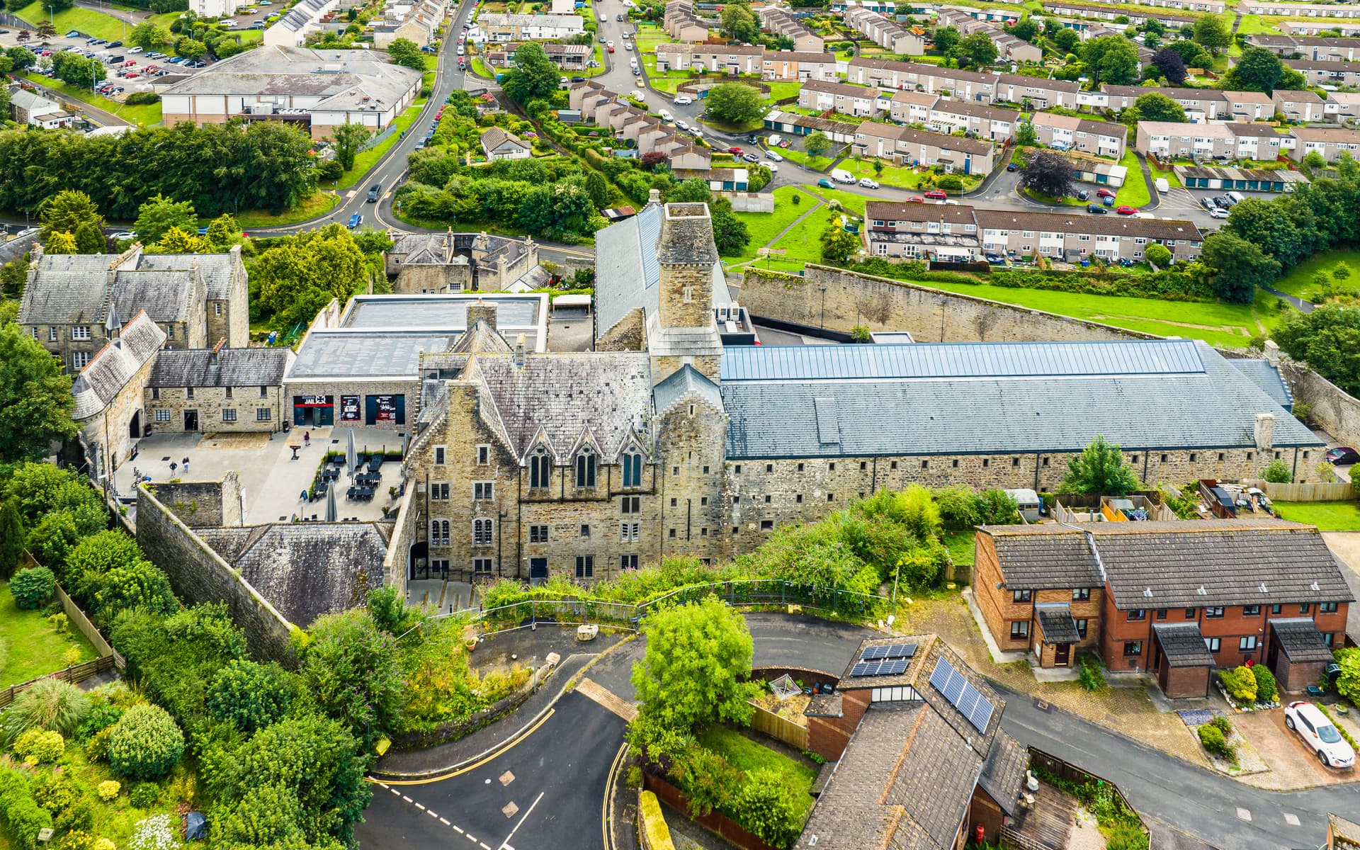 Aerial view of Bodmin Jail complex surrounded by green trees and modern residential housing.