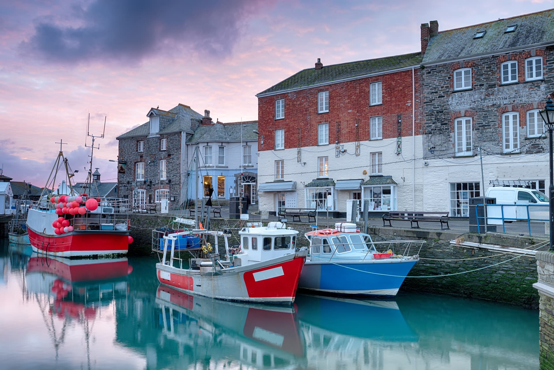 Fishing boats moored in Padstow Harbour against historic buildings at sunset.