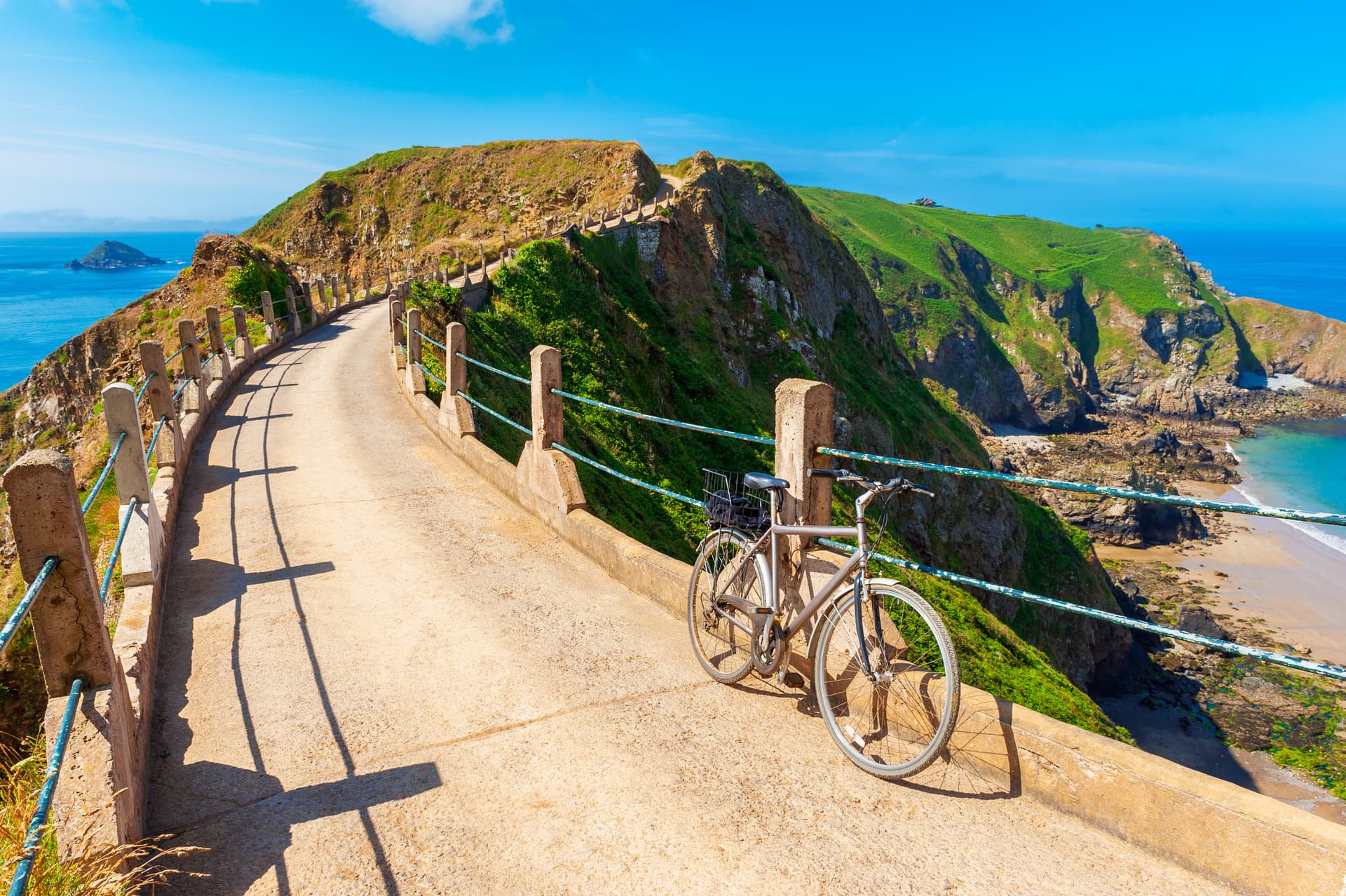 Bicycle parked on coastal path overlooking green cliffs and blue sea under bright sun