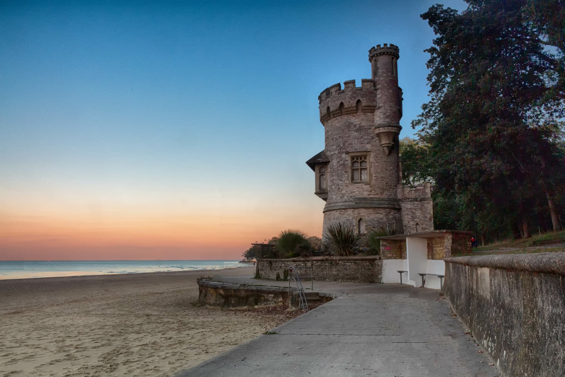 Stone tower structure beside a sandy beach at sunset with blue and orange sky