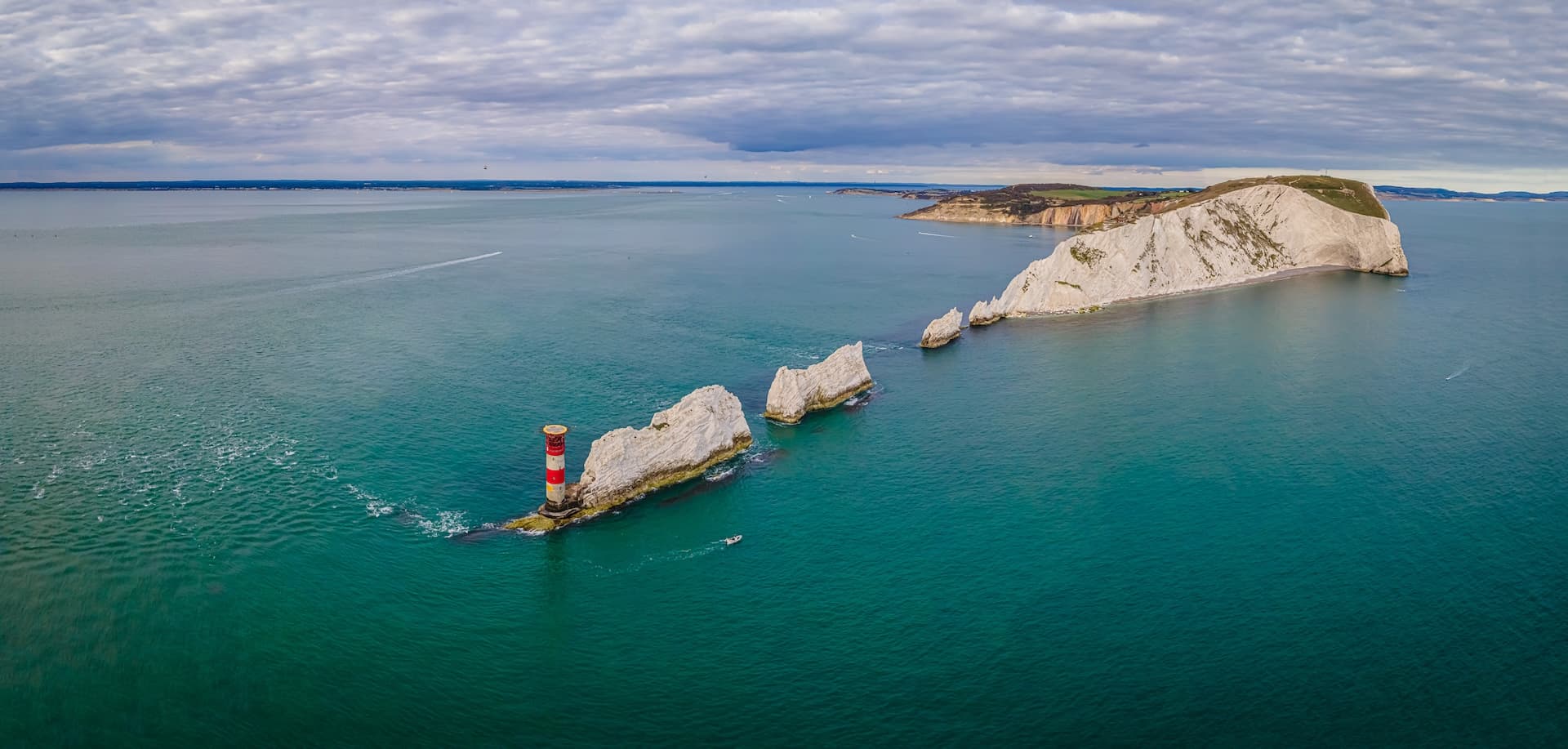 The Needles lighthouse and chalk stacks in turquoise sea water under cloudy sky