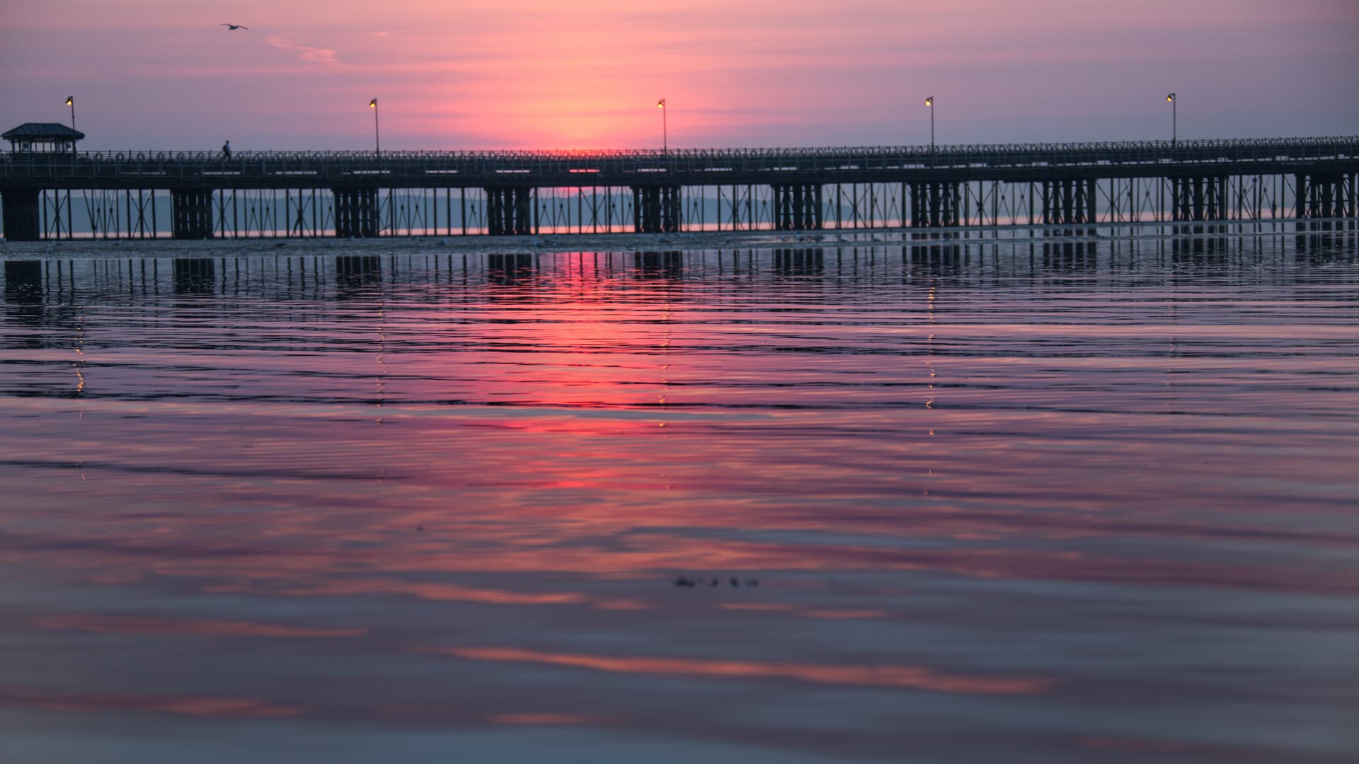 Wooden pier structure over water reflecting a pink and orange sunset sky.