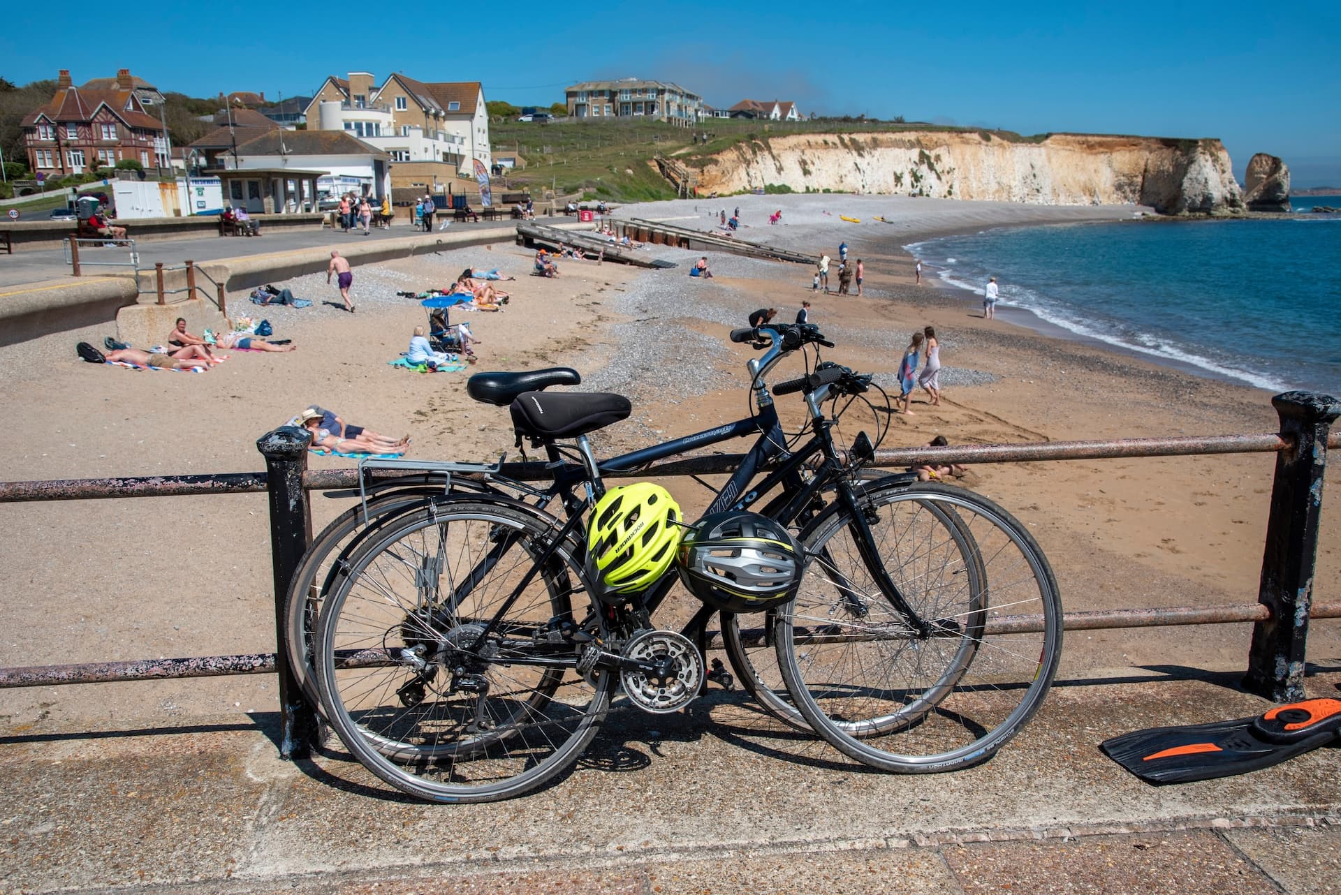 Two bicycles parked near a beach with sunbathers and chalk cliffs in the background.