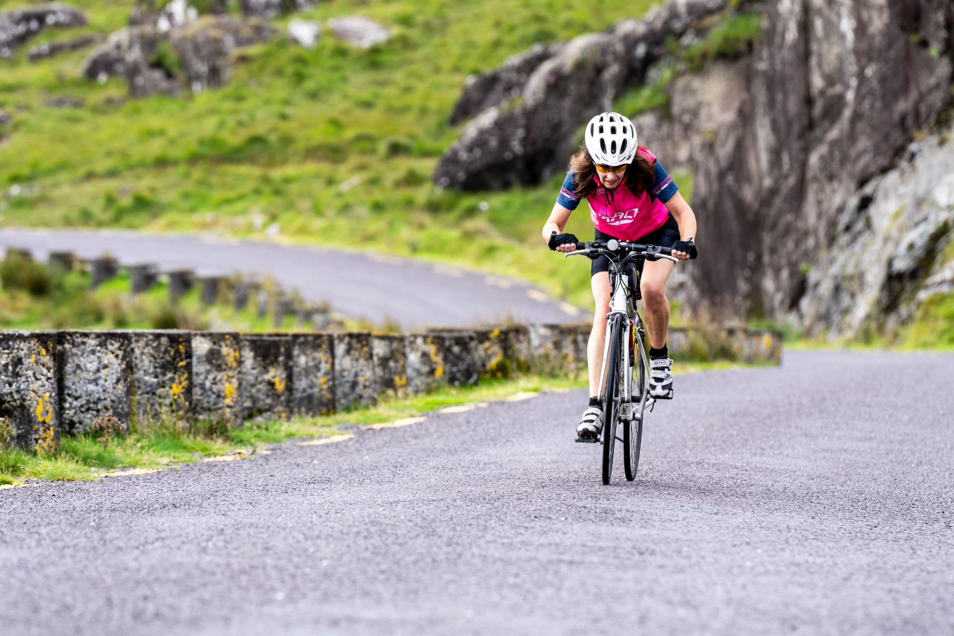 Cyclist riding on paved road with green, rocky hillsides on the Isle of Wight.