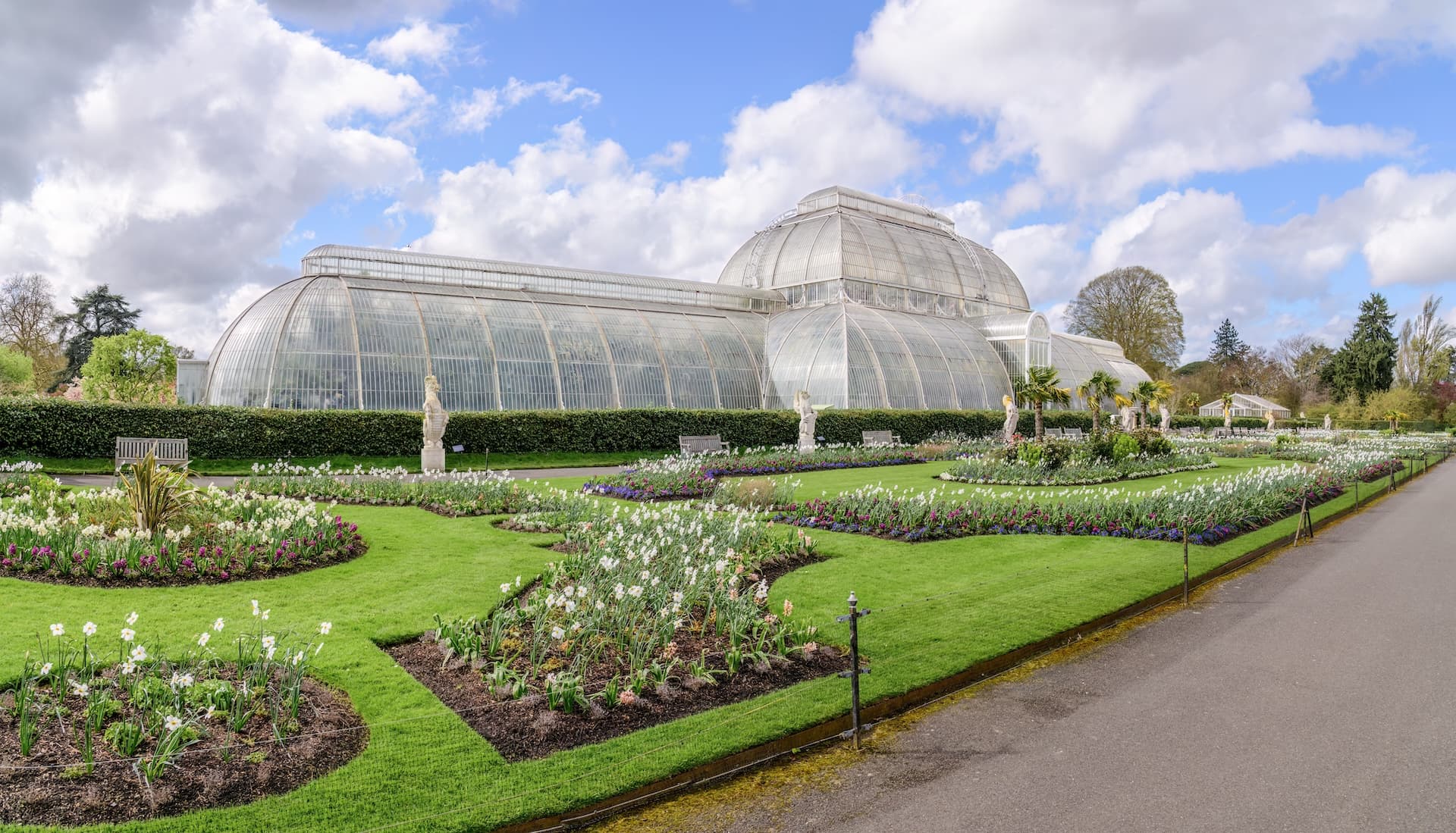 Large glass conservatory with formal flower beds and green lawn at Kew Gardens