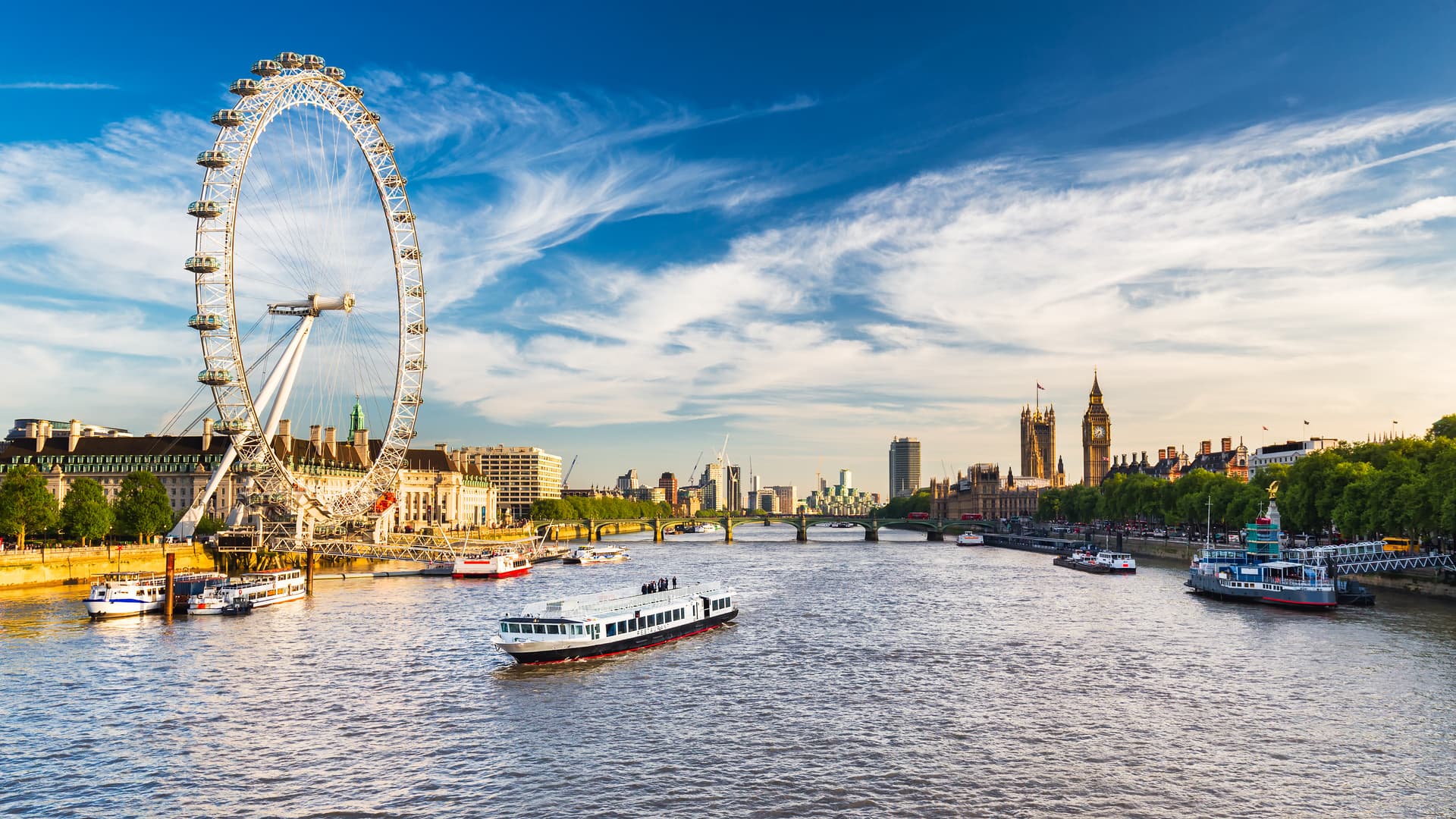 London Eye and Big Ben skyline across the River Thames with tour boats on the water.