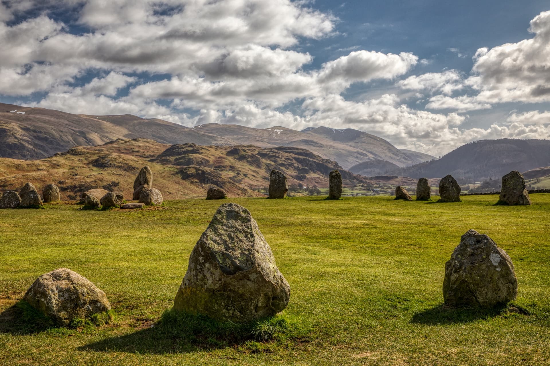Castlerigg Stone Circle with standing stones on green grass against rolling hills and cloudy sky.