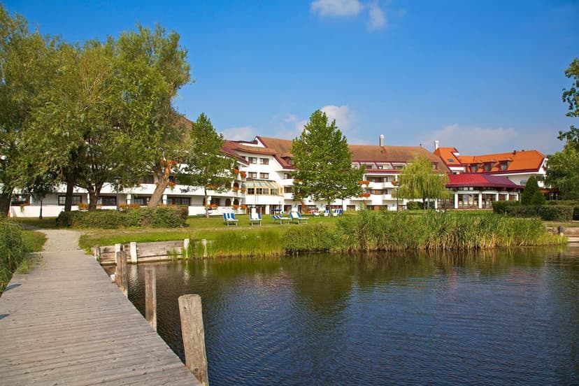 Seehotel Rust on lake with wooden dock and green lawn chairs under blue sky.
