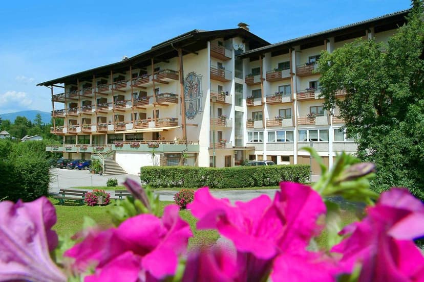 Hotel Kanz building with balconies, seen through bright pink foreground flowers, with mountains in background.