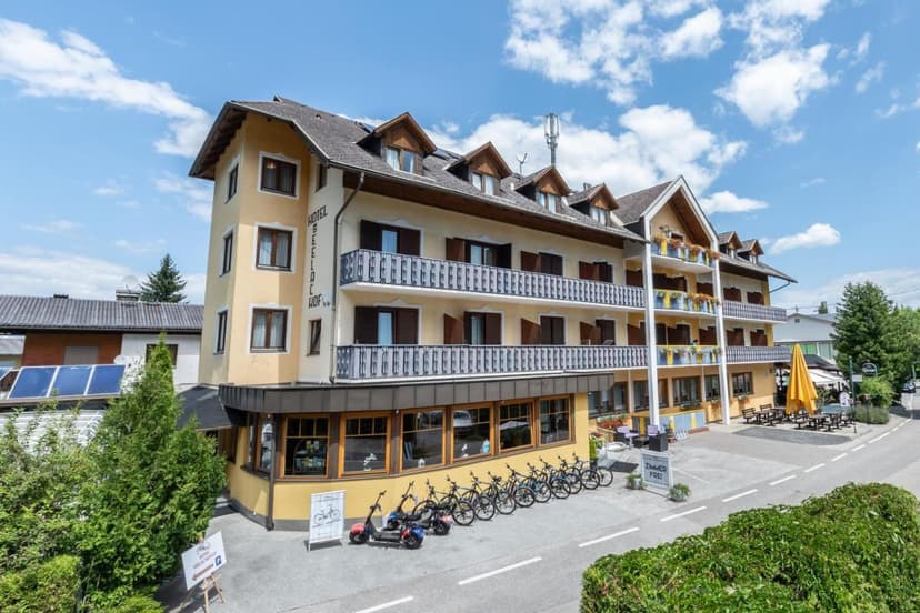 Hotel Seelacherhof building with balconies, parked bicycles, and scooters under a blue sky.