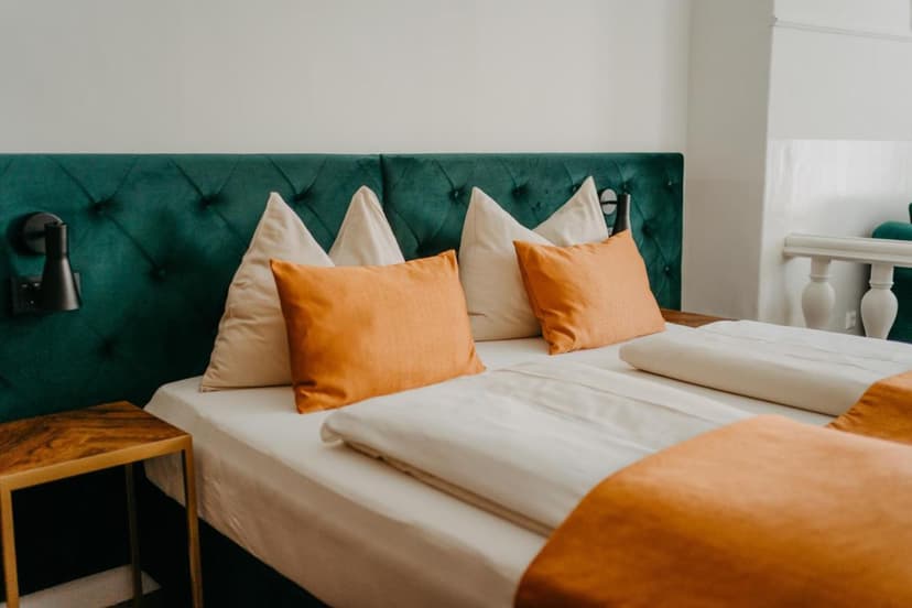 Hotel room bed with green tufted headboard, white linens, and orange accent pillows