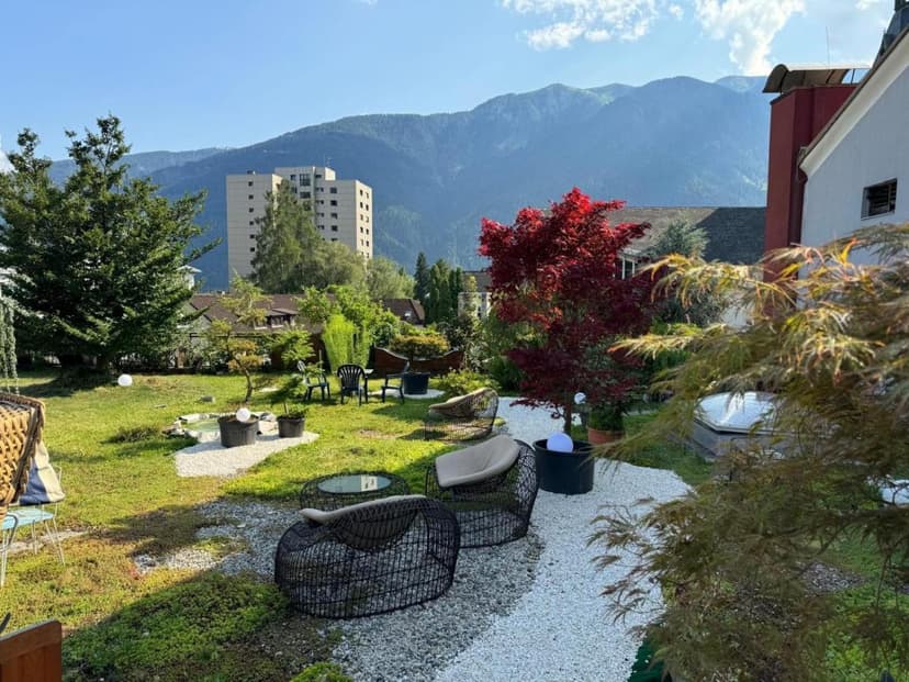 Garden seating area with modern chairs, red maple tree, and large mountains in background