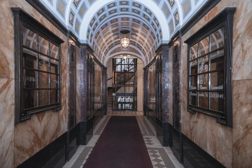 Ornate interior hallway with marble walls, vaulted ceiling, and wrought iron gate leading to stairs.