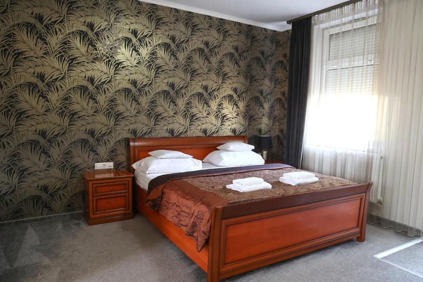 Hotel room with wooden bed, white linens, and black and gold palm leaf wallpaper.