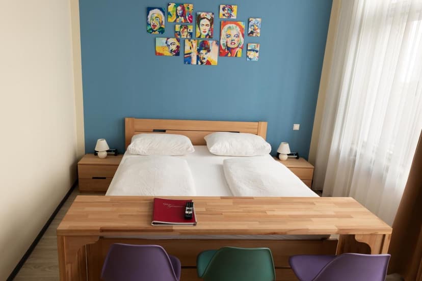 Bedroom with wooden furniture, white bedding, blue accent wall, and pop art portraits.