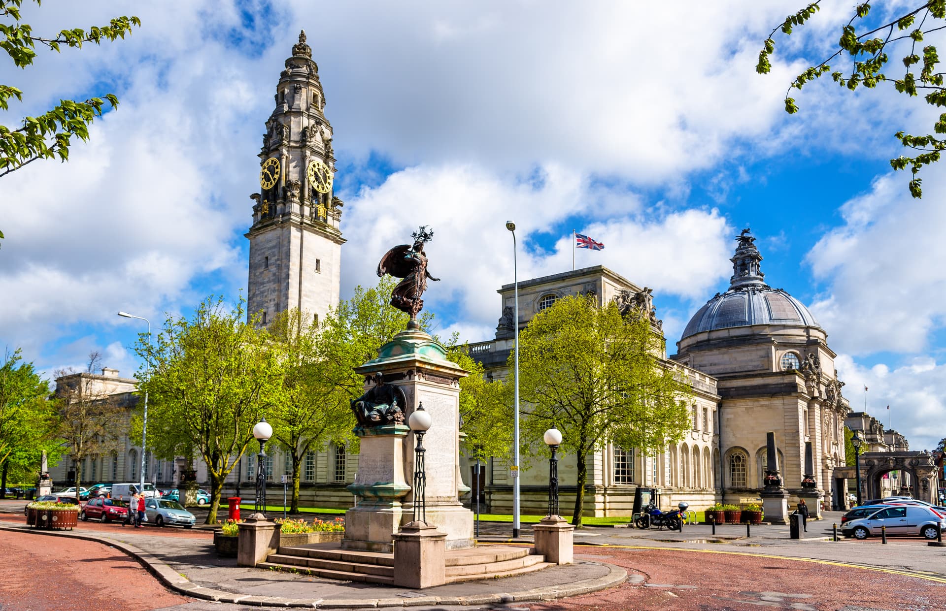 Cardiff City Hall clock tower, statue, and dome under a blue, cloudy sky.