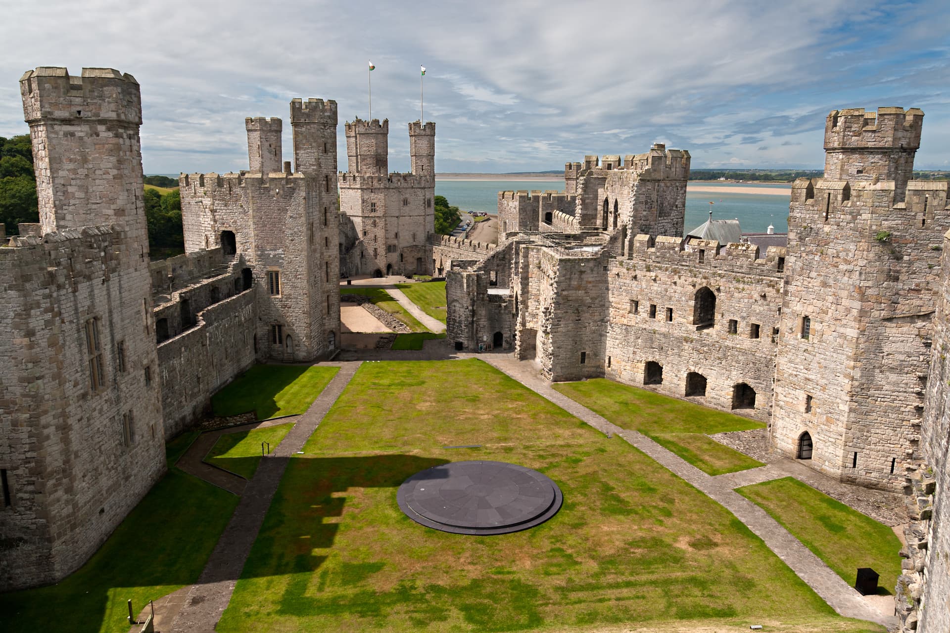 View from above of Caernarfon Castle courtyard with stone towers and green lawn near the water.