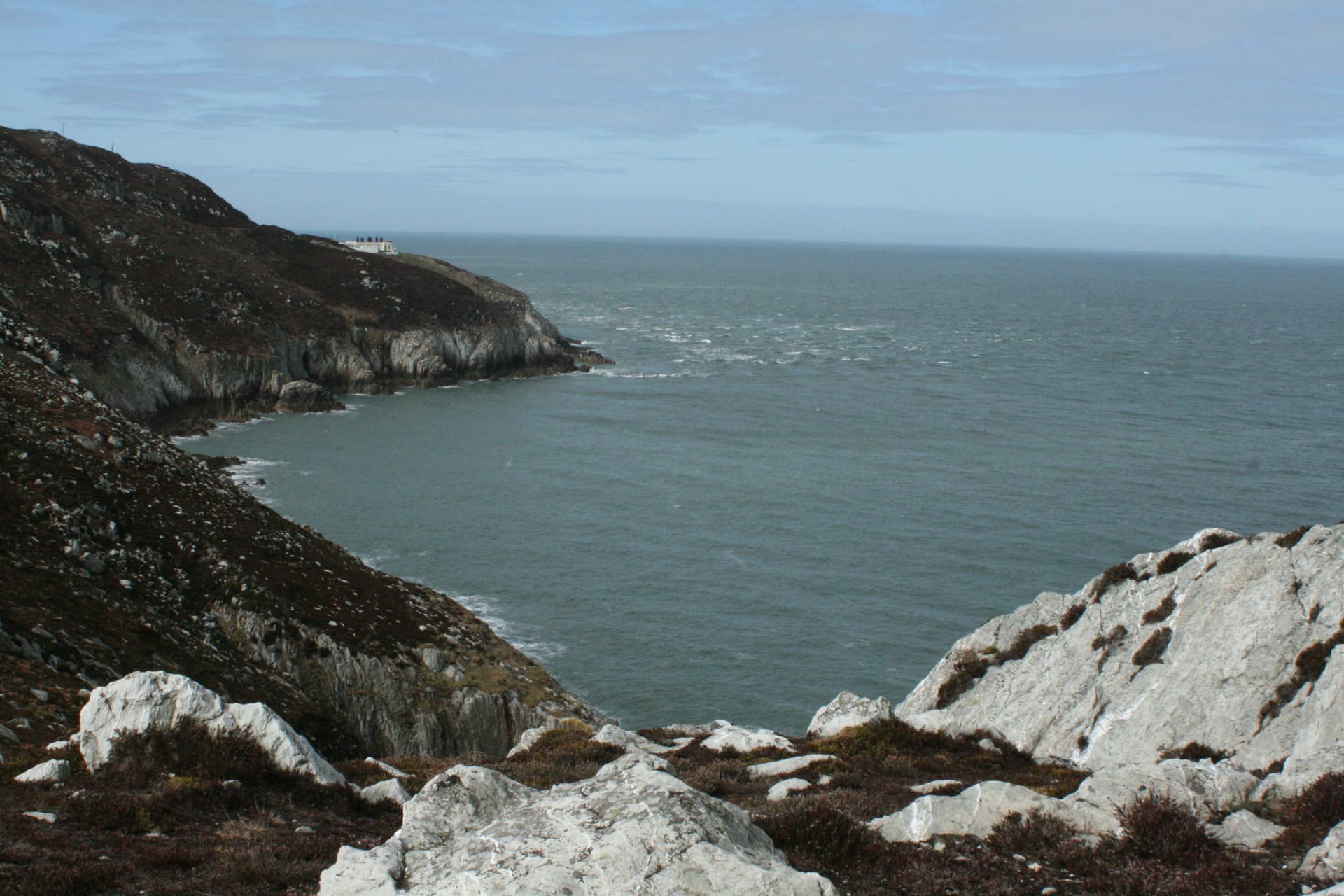 Rocky coastal cliffs meeting dark, choppy sea under a pale blue sky, Holyhead.