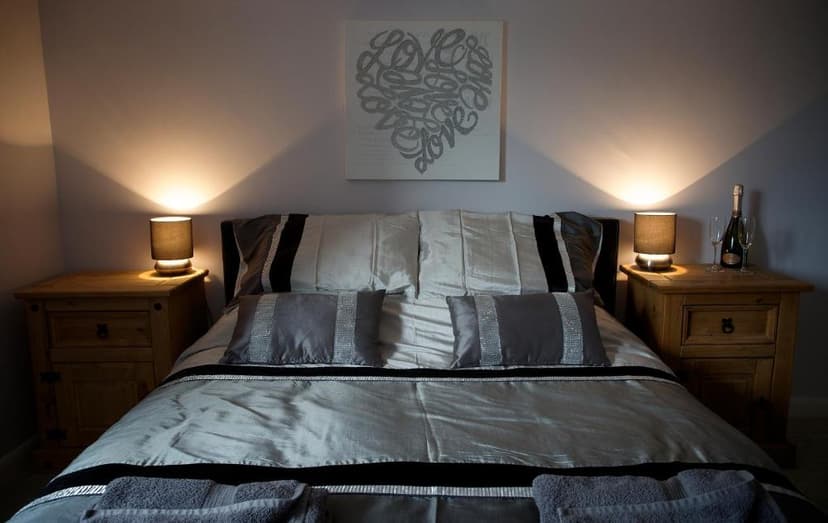 Bedroom with silver bedding, illuminated lamps, and a heart artwork above the bed