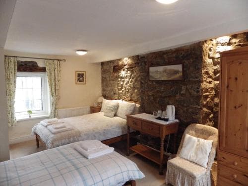 Twin bedroom in Aber Cottage B&B with stone feature wall, wooden furniture, and window.