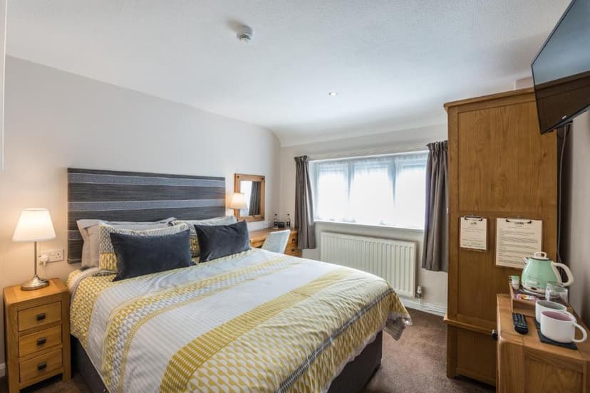 Bedroom with yellow and white patterned duvet, wooden furniture, and bright window.