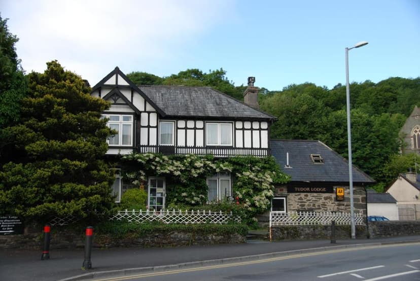 Tudor Lodge building with black and white timber framing and flowering vines beside a road.