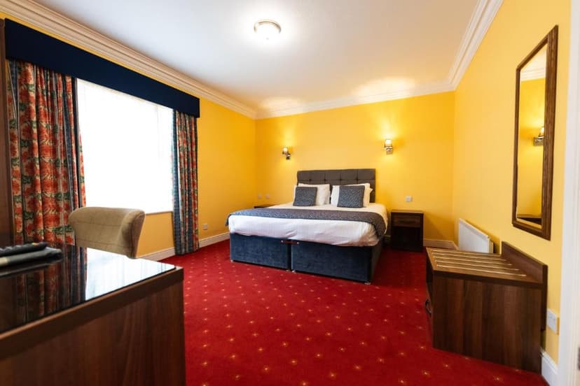Hotel bedroom with yellow walls, red patterned carpet, and a large bed.