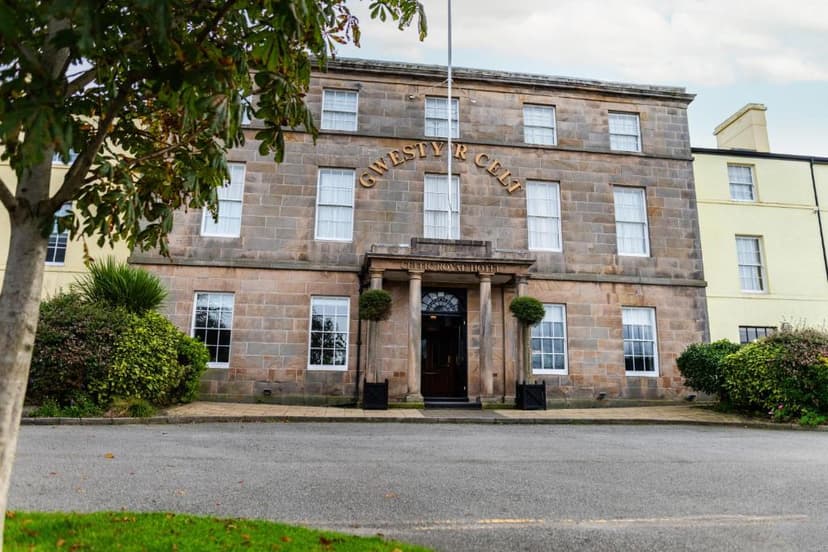 Stone Celtic Royal Hotel entrance with portico, white windows, and surrounding greenery.