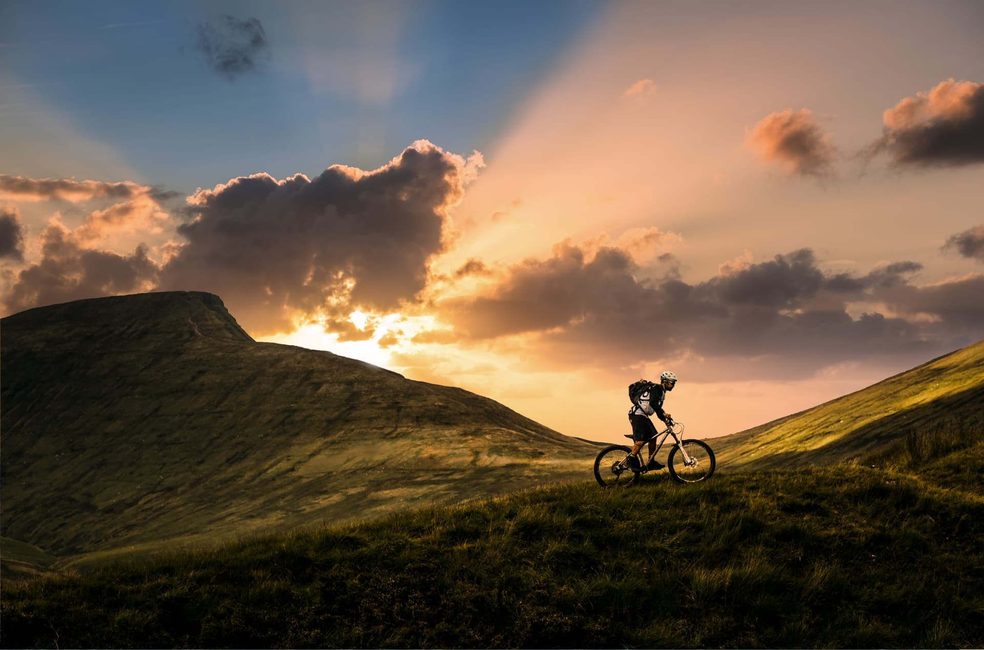 Mountain biking on grassy hills at sunset in Wales with dramatic clouds.