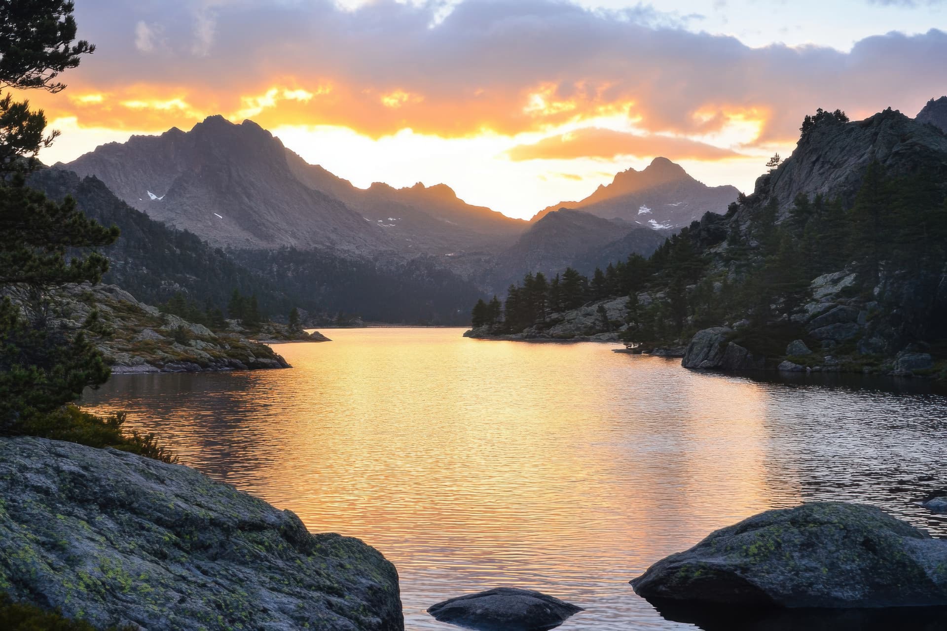 Alpine lake reflecting sunset light with rugged mountains and pine trees surrounding the shore.