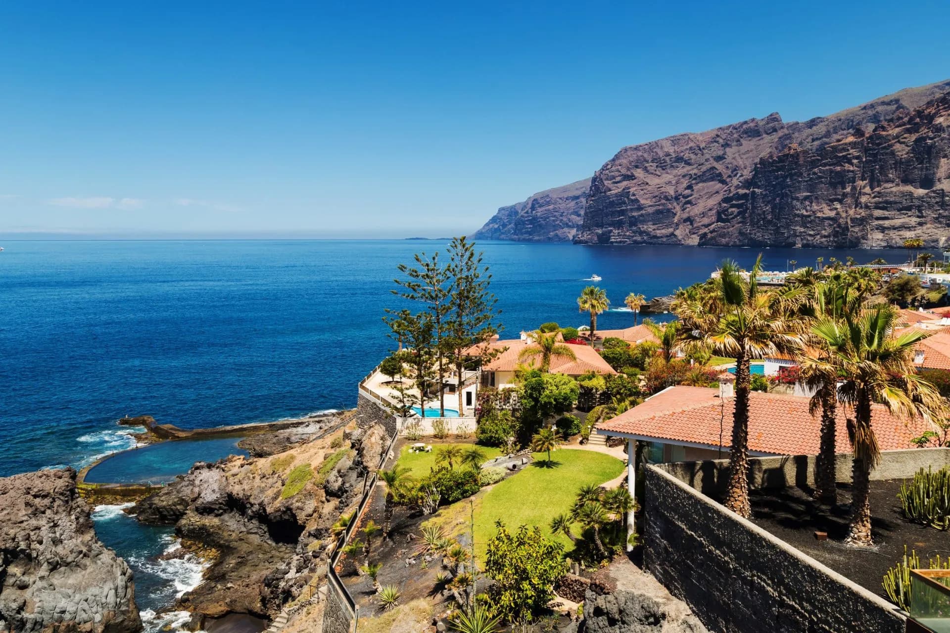 Giant rock formations of Acantilados de los Gigantes above blue sea with resort villas in Tenerife.