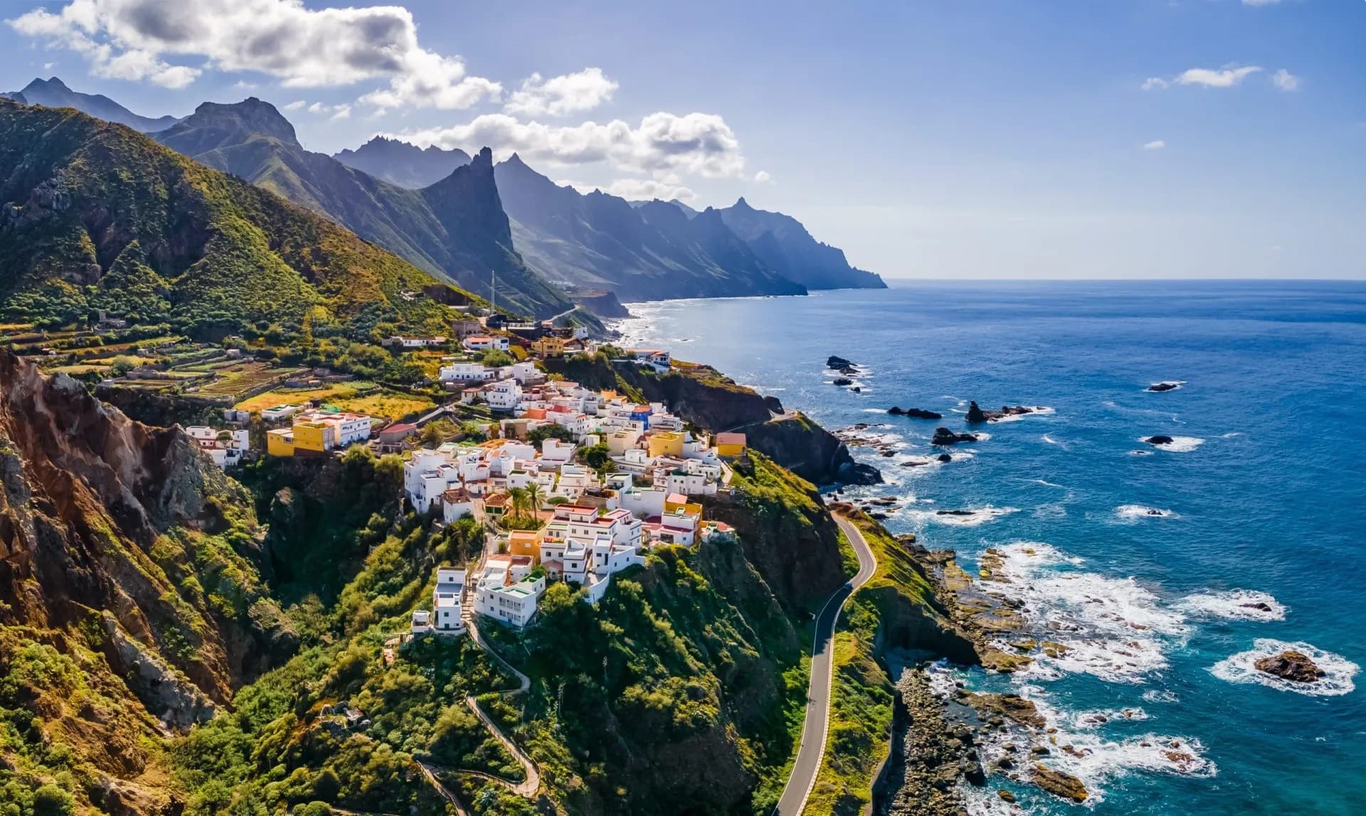Coastal village with white houses nestled on green cliffs overlooking the deep blue sea at Tenerife, Canary Islands.