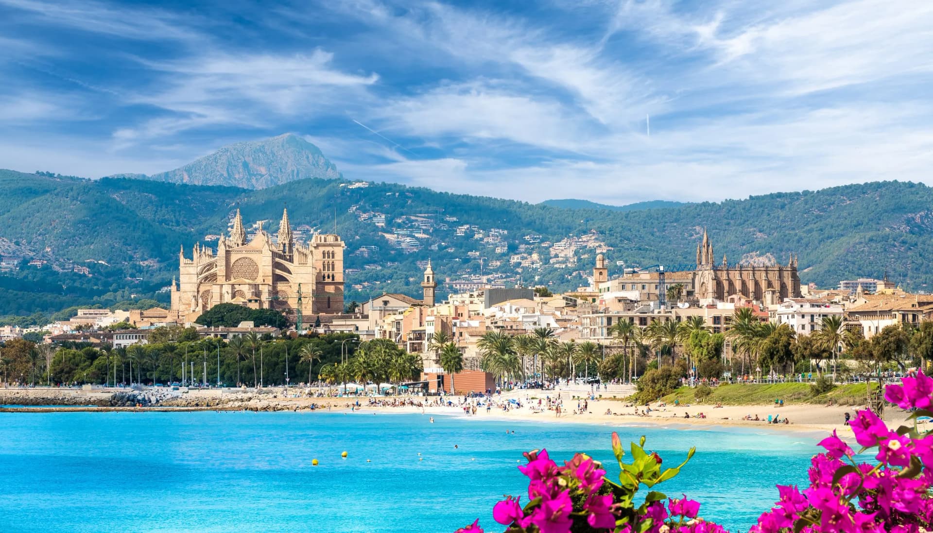 Beach and Palma de Mallorca town with cathedral, mountains, and turquoise water.
