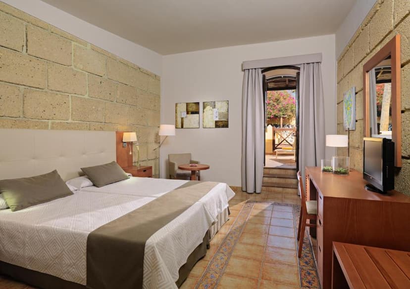 Hotel room with twin beds, stone wall texture, and balcony view of flowering trees in Salamanca.