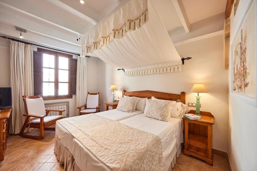 Twin beds with white canopy in a bright hotel room with wooden furniture and tile floor.