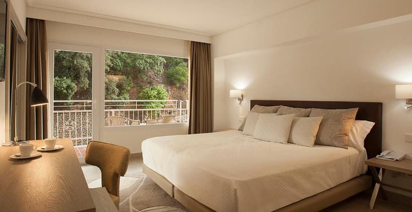 Hotel bedroom with large bed, desk, and balcony view of lush green hillside in Valldemossa.