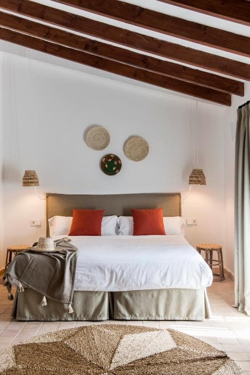 Bedroom with white linens, orange pillows, exposed wood beams, and woven wall decor at Curolla Petit Hotel.