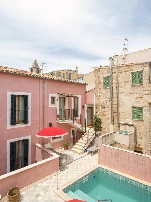 Courtyard with small pool, pink and stone buildings, and church towers in the background, Palau.