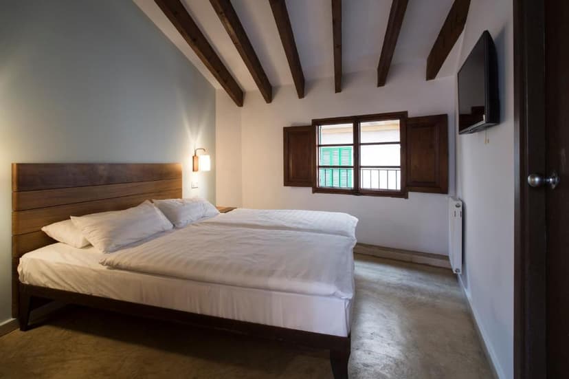 Bedroom with white linens, wooden headboard, exposed ceiling beams, and window with wooden shutters.