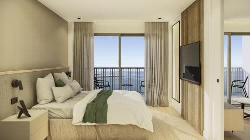 Modern hotel bedroom with white bedding and balcony overlooking the sea.