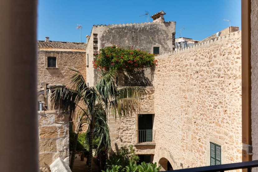 Stone buildings with palm trees and red flowers under a clear blue sky in Alcudia.