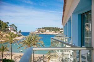 Balcony view of a small sandy beach, turquoise cove, palm trees, and distant green hillside.