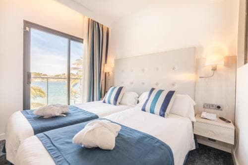 Twin hotel room with blue bedding and balcony view of the sea and palm trees