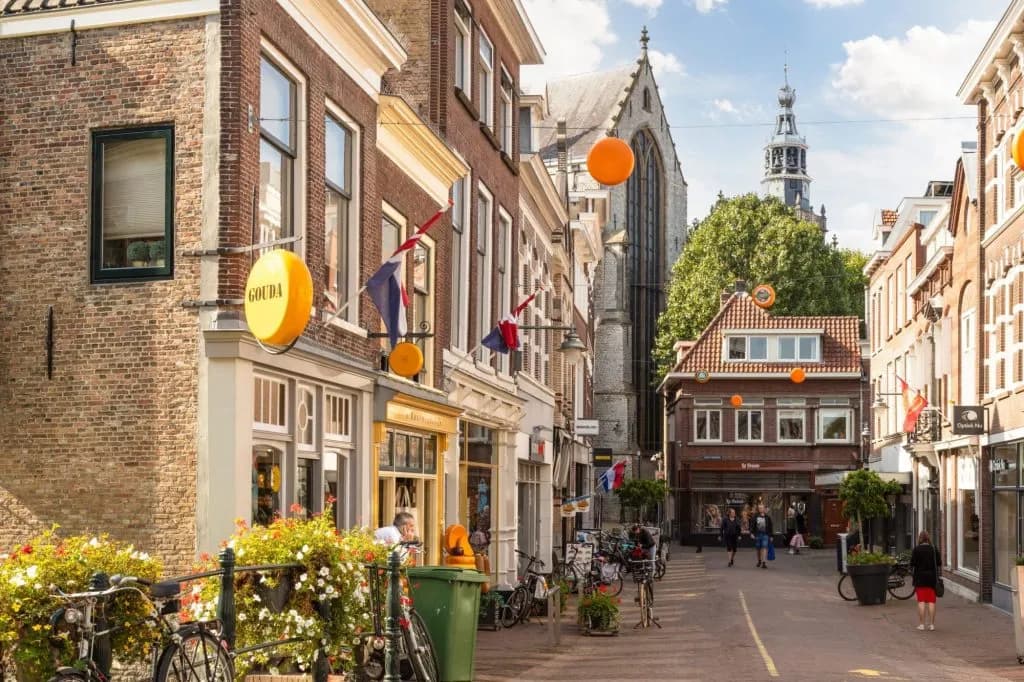 Gouda cheese shop sign on brick building in historic Dutch town street with church tower.