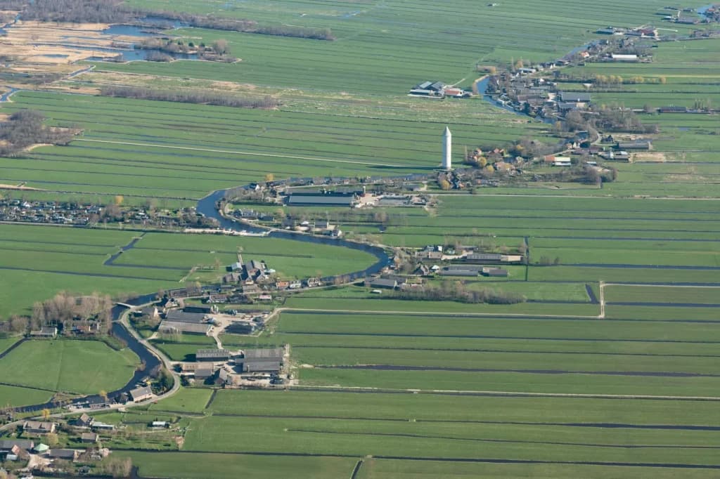 Aerial view of Nieuwkoop with a winding river, green polder fields, and a tall water tower.