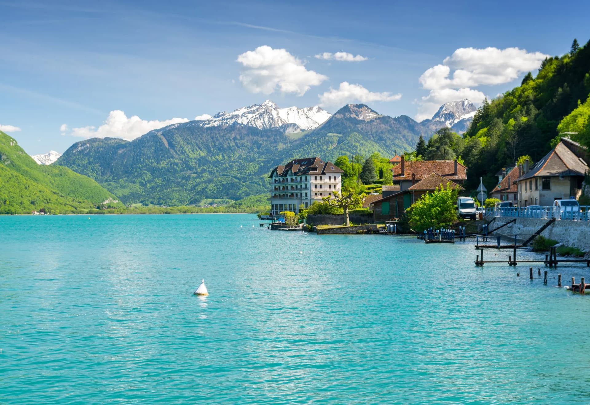 Turquoise lake in spring with snow-capped mountains and lakeside buildings in the French Alps.